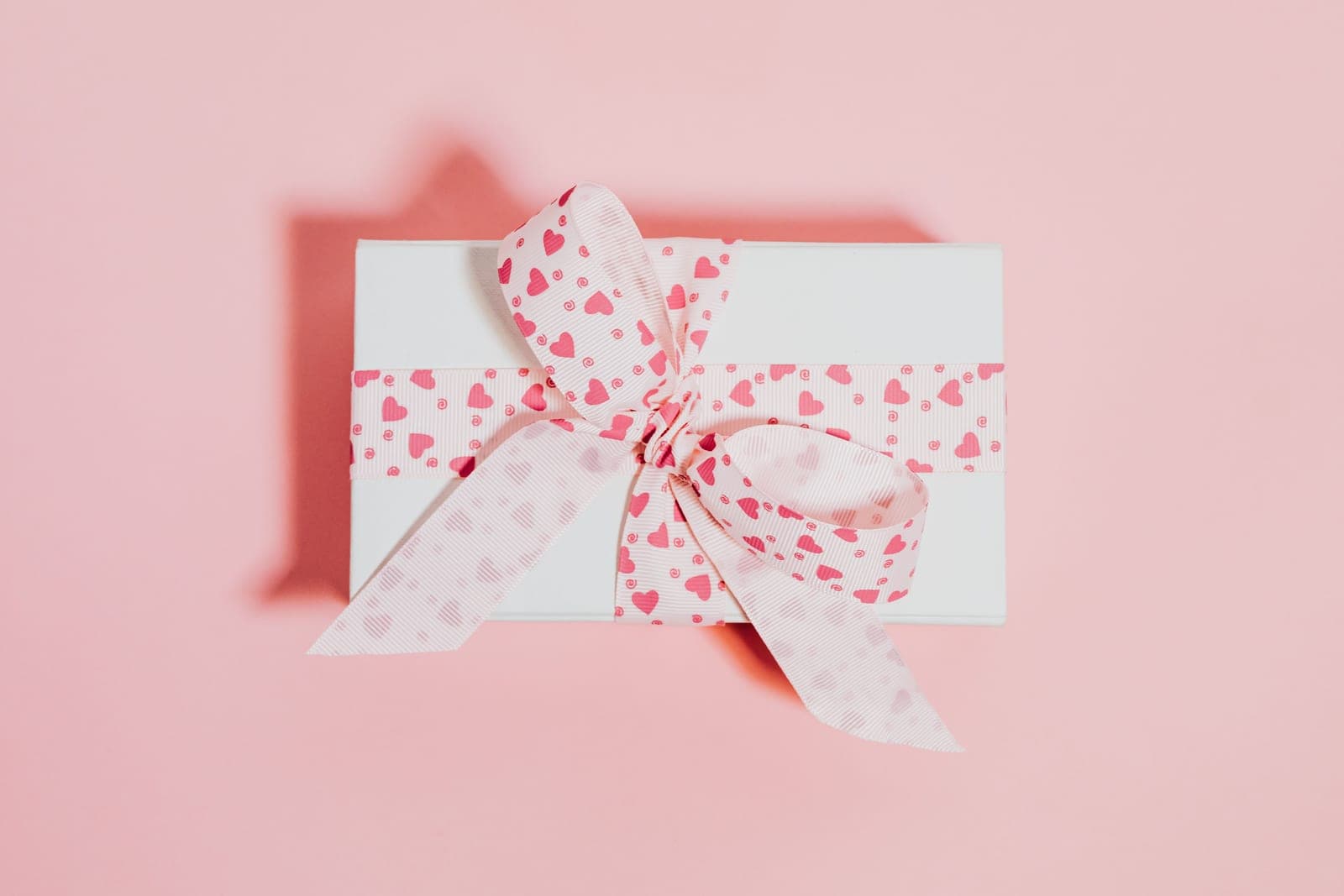 A neatly wrapped present with a ribbon on a soft blush surface